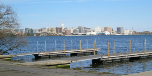 View of a city skyline across a lake, with docks in the foreground and clear blue skies above.