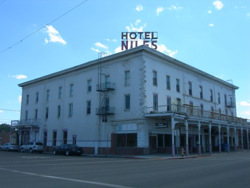 Historic building with "Hotel Niles" sign, featuring a fire escape and storefronts below, set against a blue sky.