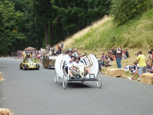 A fun soapbox race with creative homemade carts on a winding road, surrounded by spectators and greenery.