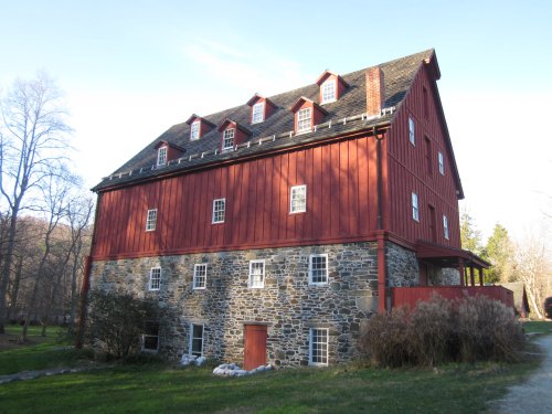 A large red barn with a stone base and multiple windows, set in a grassy area with trees in the background.
