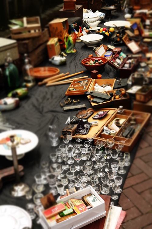 A cluttered market table filled with various antiques, glassware, and collectibles.