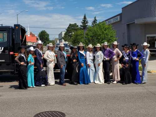 A group of women in colorful western attire and cowboy hats poses together in a sunny street.