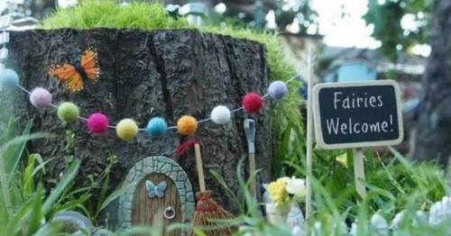 A whimsical fairy door on a tree stump, surrounded by colorful decorations and a sign that says "Fairies Welcome!"