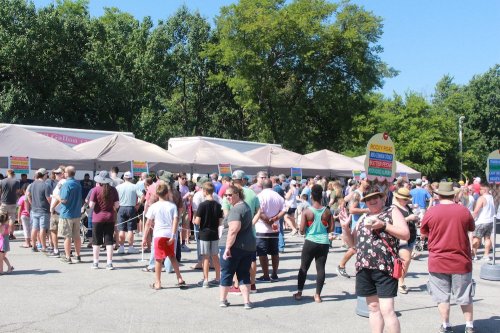 A large crowd gathers at outdoor tents, enjoying a sunny day at a festival or event.