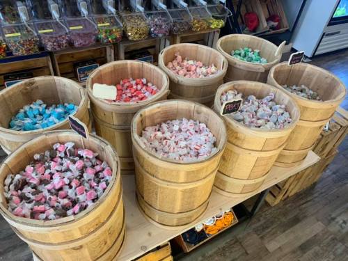 Colorful candy displayed in wooden barrels, featuring various types and flavors in a sweet shop setting.