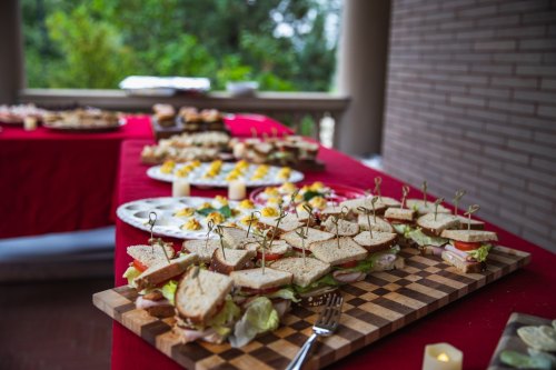 A table set with sandwiches on a wooden board and assorted appetizers on plates, surrounded by greenery.