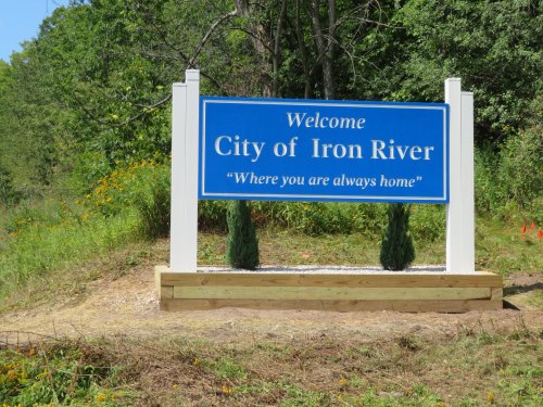 Welcome sign for the City of Iron River, featuring the slogan "Where you are always home," surrounded by greenery.