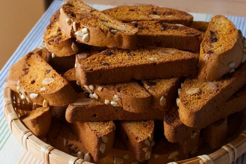 A basket filled with golden-brown biscotti, studded with almonds and chocolate, stacked neatly.