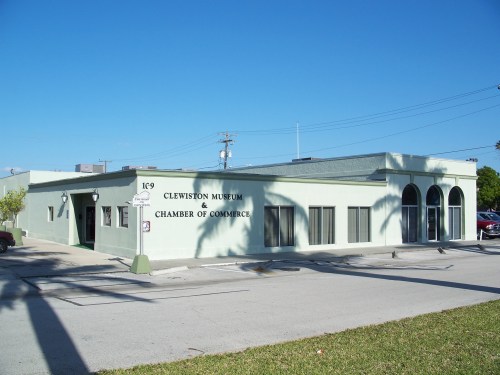 Exterior view of the Clewiston Museum and Chamber of Commerce building, featuring a light green facade and arched windows.