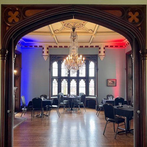 Elegant dining room with chandeliers, black tables, and blue and red lighting, framed by an ornate archway.