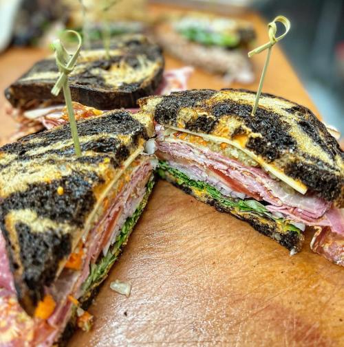 A close-up of a sliced sandwich with layers of meats, cheese, and vegetables, held together with toothpicks on a wooden board.