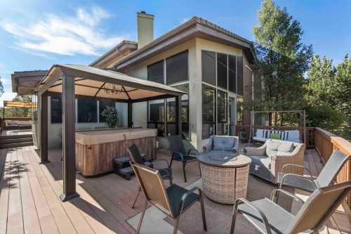 A spacious outdoor deck with a hot tub, seating area, and a view of trees under a clear blue sky.