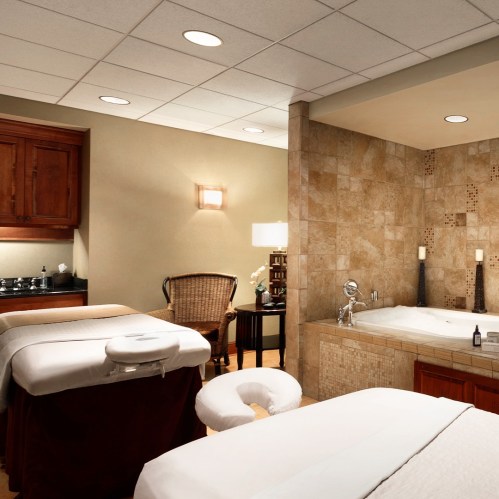 A serene spa room featuring massage tables, a soaking tub, and warm lighting for relaxation.