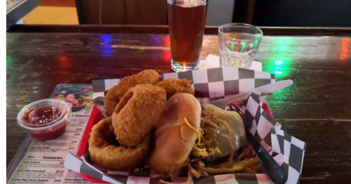 A tray with a cheeseburger, onion rings, and a side of ketchup, accompanied by a glass of beer and a shot of whiskey.