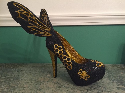 A black and gold high-heeled shoe with glitter and decorative wing-like accents.