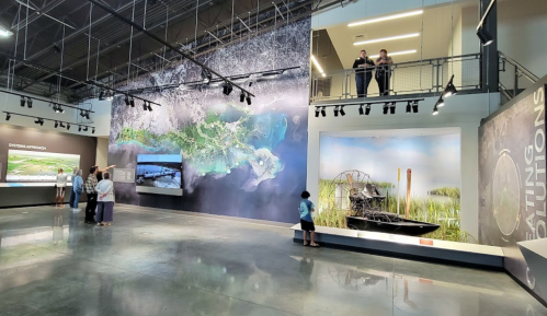 Visitors explore an exhibit featuring large maps and displays about wetlands and airboats in a spacious gallery.