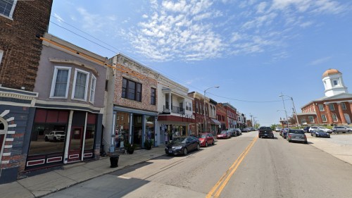 A street view of a small town with historic buildings, shops, and parked cars under a clear blue sky.