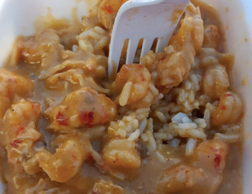 A close-up of shrimp and rice in a creamy sauce, with a white fork partially submerged in the dish.