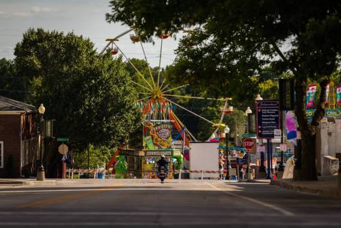 A street view leading to a colorful carnival with a Ferris wheel and festive decorations in the background.
