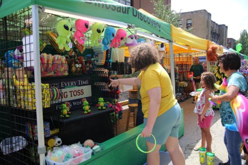 A vibrant outdoor market with colorful stalls, featuring toys and games. Children and adults engage in fun activities.