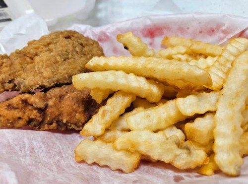A plate of crispy fried chicken strips next to a serving of crinkle-cut French fries.