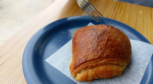 A golden-brown croissant on a blue plate with a fork resting nearby.