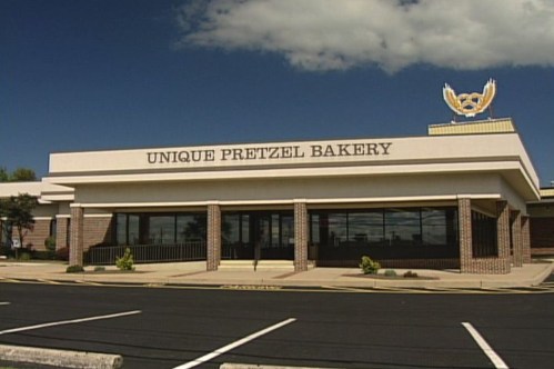Exterior of Unique Pretzel Bakery, featuring a sign with a pretzel logo and a clear blue sky in the background.