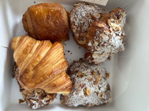 A box of assorted pastries, including a croissant, almond pastry, and a glazed pastry.
