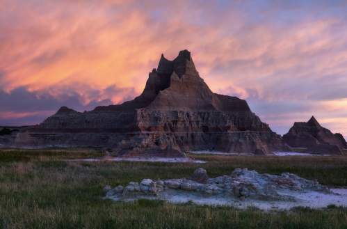 A dramatic rock formation rises against a colorful sunset sky, surrounded by grassy terrain.