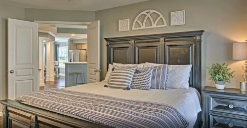 Cozy bedroom featuring a dark wood bed, striped bedding, and soft lighting, with an open doorway to a kitchen area.