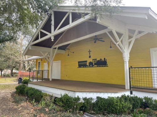 A yellow building with a covered stage, featuring a train silhouette on the wall and greenery in front.