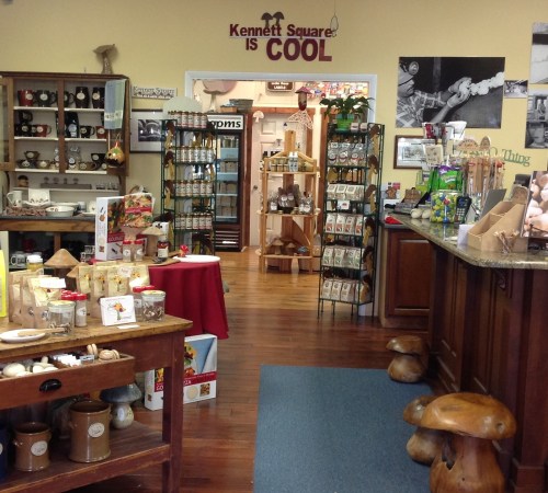 Interior of a cozy shop featuring local products, wooden displays, and a welcoming atmosphere. "Kennett Square is COOL" sign visible.