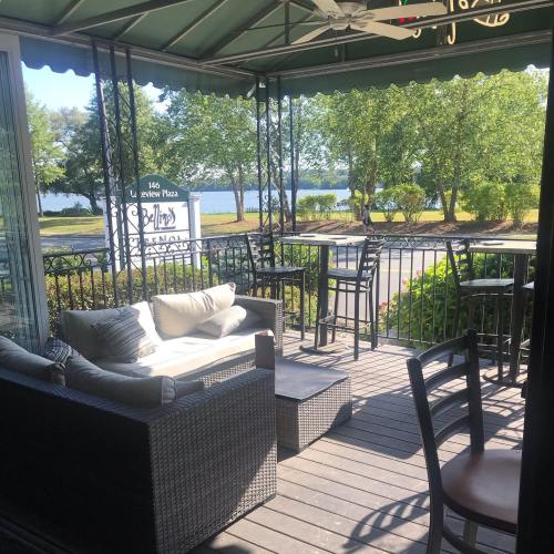 A cozy outdoor seating area with a sofa and tables, overlooking a lake surrounded by trees.