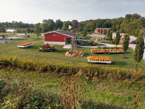 A scenic farm with a red barn, decorated with pumpkins and autumn plants, surrounded by green fields and trees.