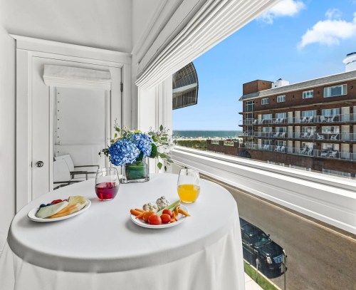 A table with a floral centerpiece and two drinks, overlooking a scenic view of buildings and a blue sky.