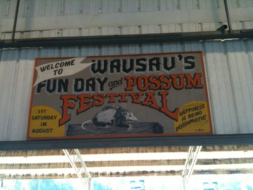 Sign welcoming visitors to Wausau's Fun Day and Possum Festival, featuring a possum illustration and event details.