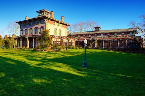 Historic mansion with ornate architecture, surrounded by lush green grass and clear blue sky.