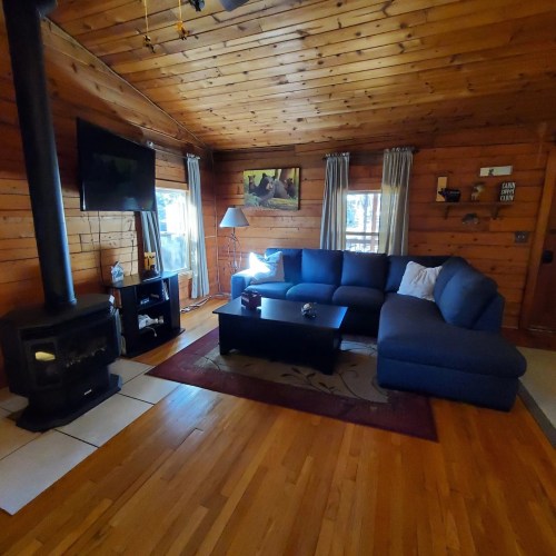Cozy wooden living room with a blue sectional sofa, TV, and a warm atmosphere, featuring a rug and large windows.