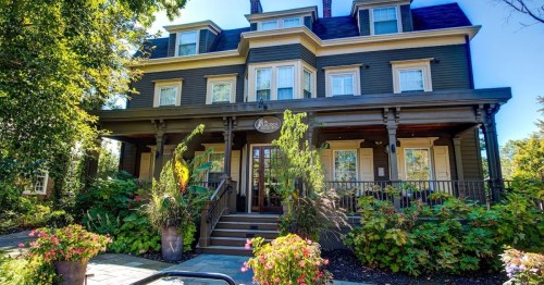 A large, elegant house with a porch, surrounded by lush greenery and colorful flowers.