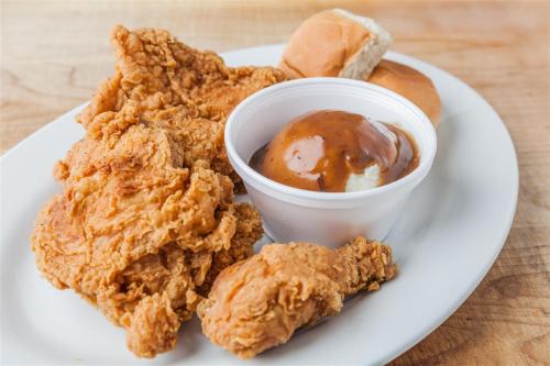 A plate of crispy fried chicken, a side of mashed potatoes with gravy, and two dinner rolls.