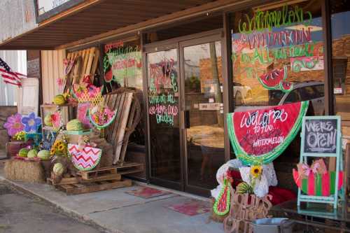 Colorful storefront decorated with watermelon-themed signs, flowers, and produce, welcoming customers inside.