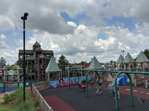 A colorful playground with a castle-like structure, swings, and children playing under a partly cloudy sky.