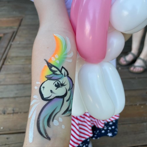 A child's arm with a colorful unicorn face painting and a balloon in the background.