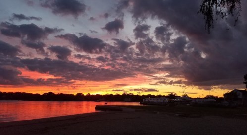 A vibrant sunset over a calm lake, with colorful clouds reflecting on the water and silhouettes of trees in the background.