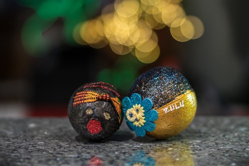 Two decorative balls, one black with a red dot and patterned ribbon, the other gold with blue flower accents, on a shiny surface.