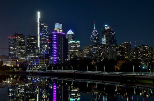 Nighttime skyline of Philadelphia with illuminated buildings reflecting in the water.