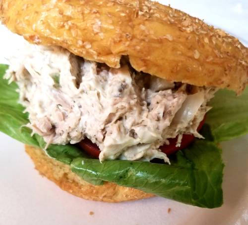 A close-up of a sandwich with a sesame seed bun, filled with chicken salad, lettuce, and tomato.