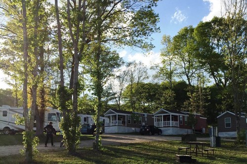 A serene campsite with several cabins and RVs surrounded by trees under a blue sky with scattered clouds.