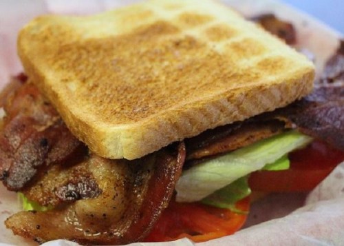 A toasted sandwich with layers of bacon, lettuce, and tomato, topped with a slice of golden-brown bread.