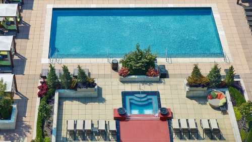 Aerial view of a swimming pool area with lounge chairs, landscaped gardens, and a hot tub.